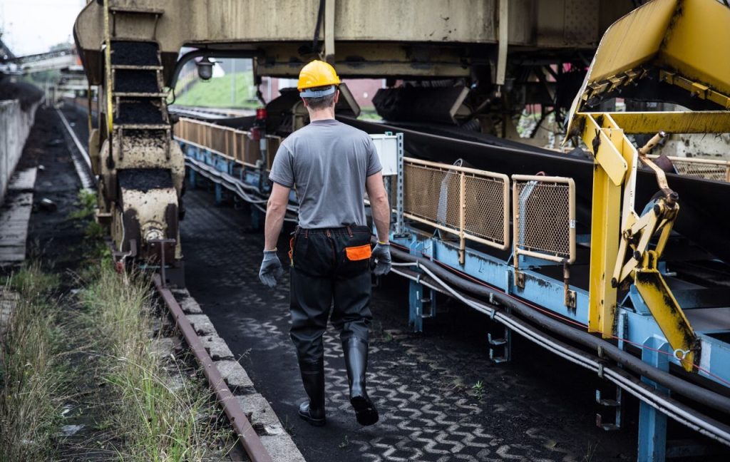 A worker in safety gear examines industrial machinery in an outdoor setting, showcasing industry work.