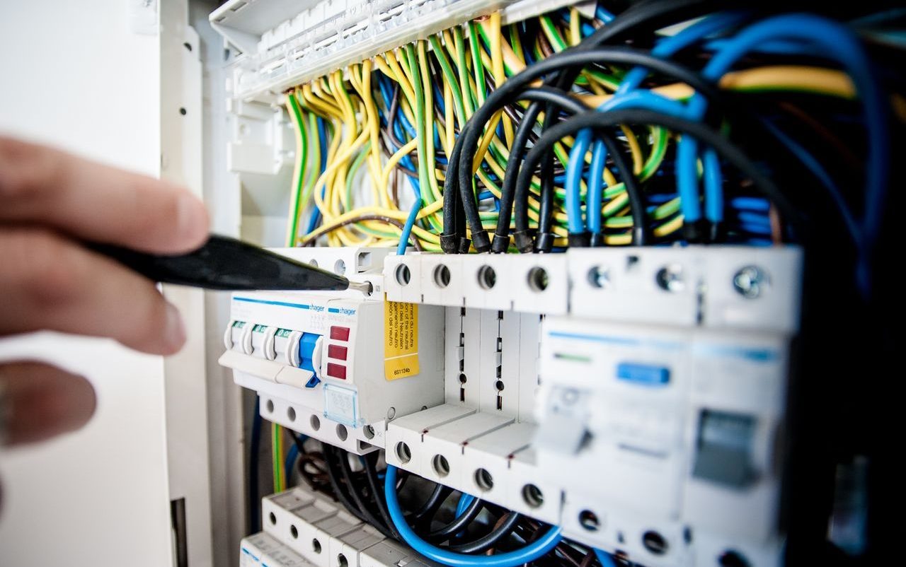 Hand of electrician working on a circuit breaker panel with colorful wires, ensuring safe electrical connections.