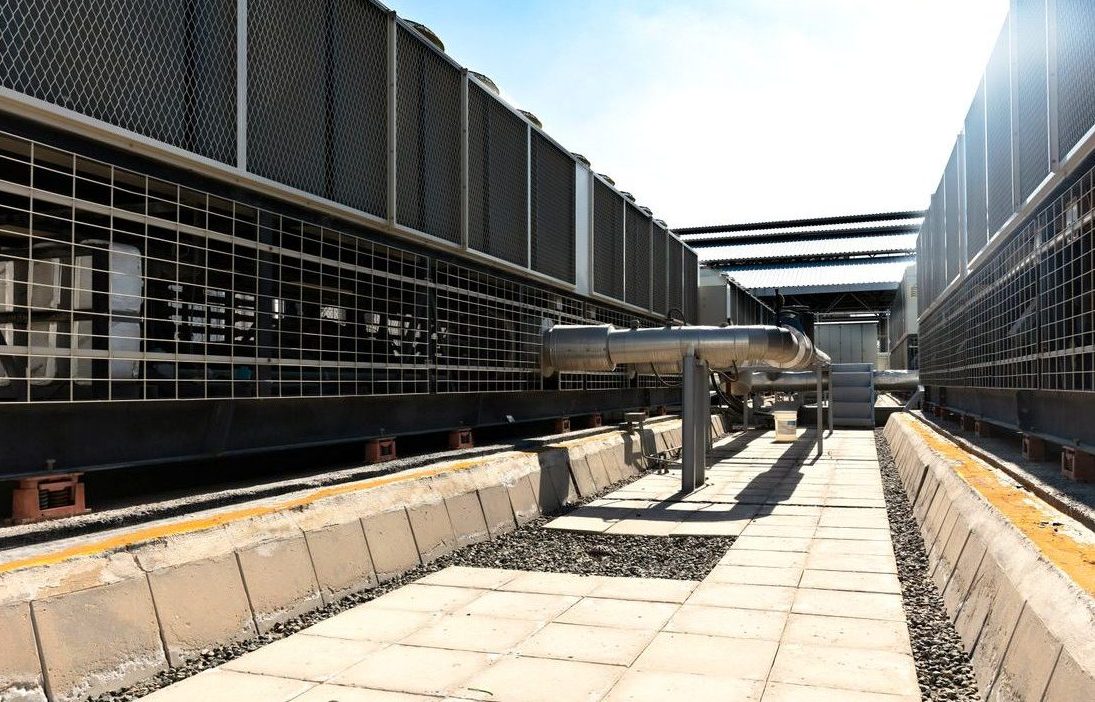 View of a large industrial cooling system with metal pipes and grids outdoors under bright daylight.